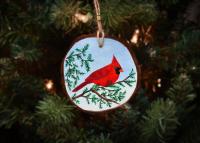 A hand-painted northern cardinal on a cedar branch on a wood slice Christmas ornament available for purchase at covecreekphotography.com.