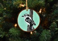 A wood slice Christmas ornament with a hand-painted downy woodpecker that is available for purchase at covecreekphotography.com.