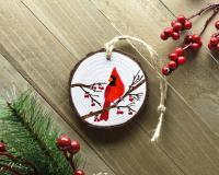 A display of an acrylic painting of a northern cardinal hand-painted on a wood slice ornament at Cove Creek Photography.