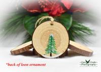 A hand-painted evergreen in the snow on the back of a common loon wood slice ornament at Cove Creek Photography.