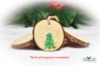 The back of a hooded merganser wood slice ornament with a hand-painted evergreen tree.