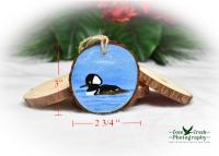 A hand-painted hooded merganser on a wood slice ornament with a diagram of ornament measurements.