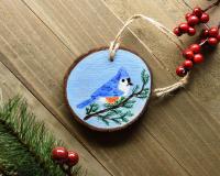 A hand-painted tufted titmouse wood slice Christmas ornament displayed on a wood background at covecreekphotography.com.