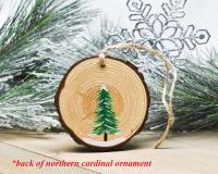 An evergreen tree in the snow hand-painted on the back of a northern cardinal ornament at covecreekphotography.com.