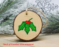 Holly leaves with red berries are hand-painted on a wood slice ornament at covecreekphotography.com.