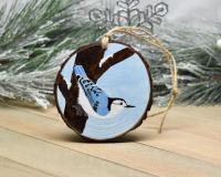 A 3.5 inch round wood slice Christmas ornament with a hand-painted white-breasted nuthatch perched on the side of a tree at Cove Creek Photography.