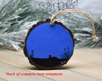 A hand-painted silhouette of a loon on a pond with a starry sky as background on a wood slice at covecreekphotography.com.