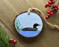 A handmade common loon wood slice Christmas ornament displayed on weathered wood at Cove Creek Photography.