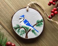 A handmade blue jay Christmas ornament displayed on a weathered wood board at Cove Creek Photography.