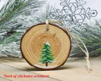 An evergreen tree in the snow is hand-painted on a wood slice the wood grain as background at covecreekphotography.com.