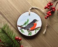 A hand-painted American robin Christmas ornament displayed on a flat wood surface at Cove Creek Photography.