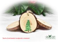 A hand-painted evergreen tree in the snow on a wood slice ornament.