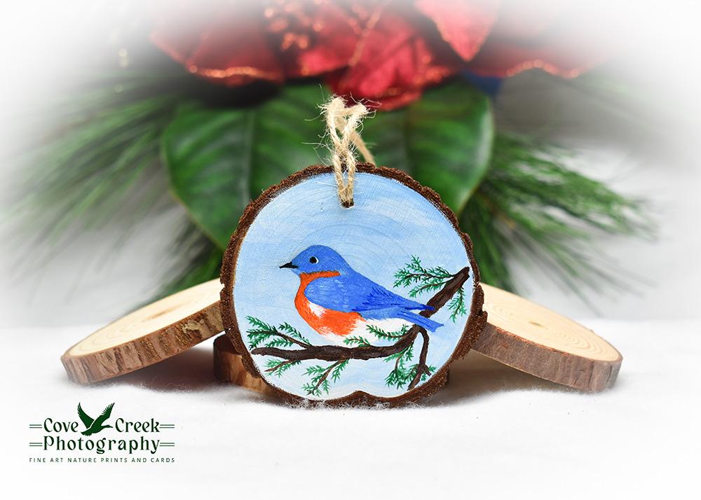 A hand-painted wood slice with an eastern bluebird on a cedar branch at Cove Creek Photography.