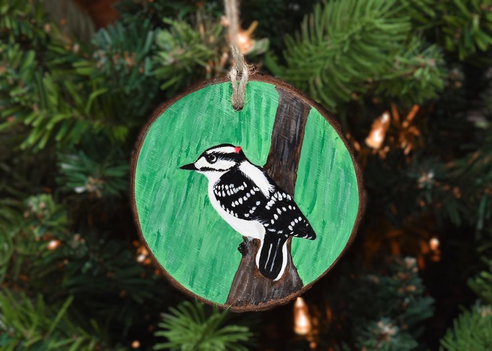 A wood slice with a hand-painted downy woodpecker hanging on a Christmas tree at Cove Creek Photography.