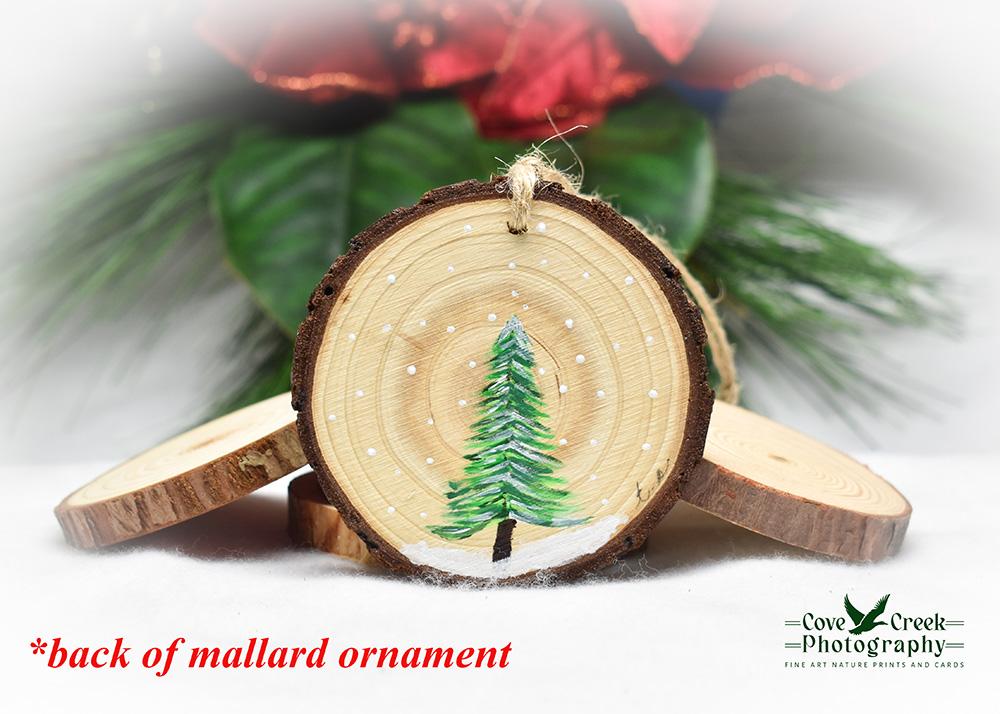 A hand-painted evergreen tree on the back of a wood slice ornament at Cove Creek Photography.