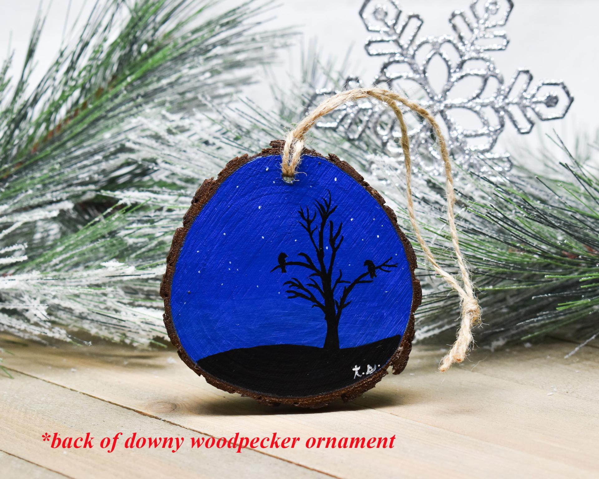A hand-painted starry winter night with a black silhouette of birds in a tree on the back of a woodpecker wood slice ornament at covecreekphotography.com.