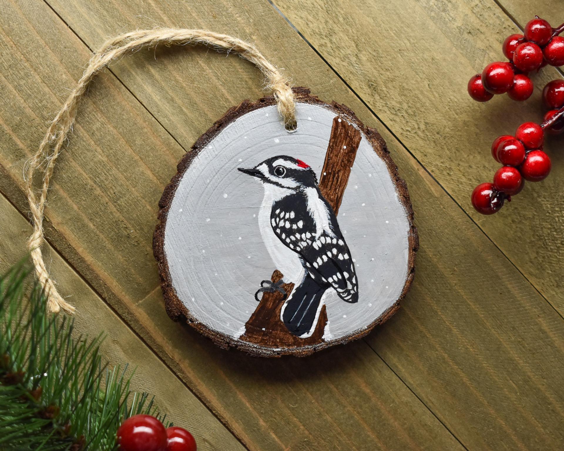 A wood slice with a handpainted downy woodpecker and winter gray background at covecreekphotography.com.