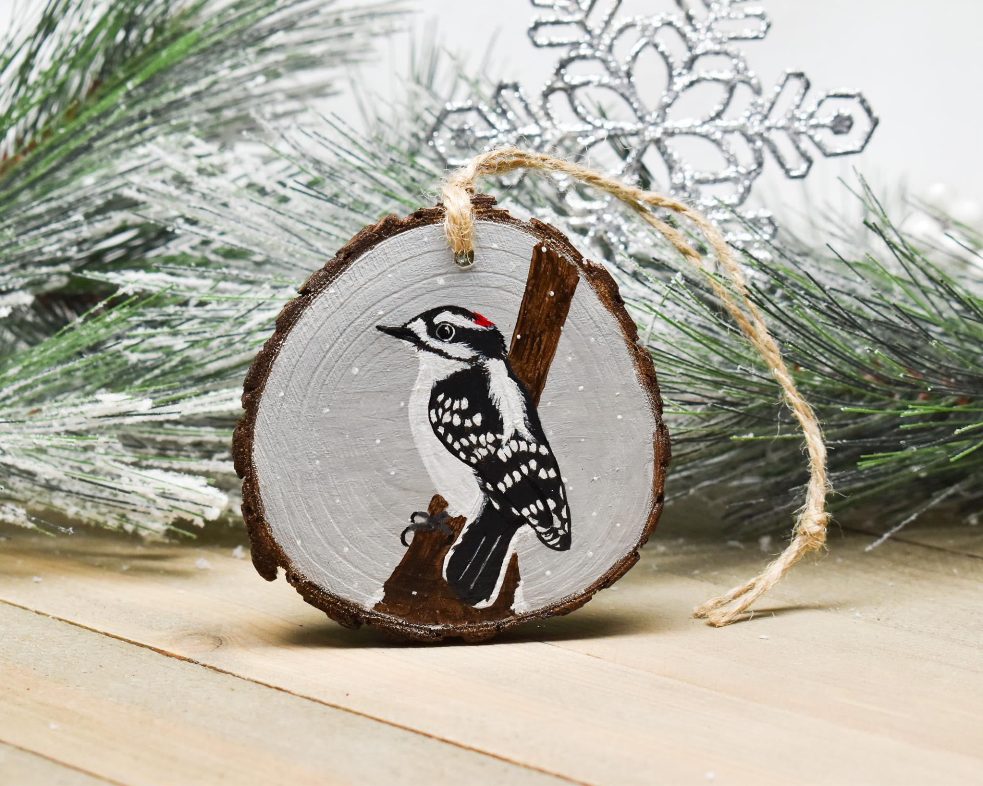 A hand-painted downy wood pecker in falling snow on a pear shaped wood slice ornament at Cove Creek Photography.