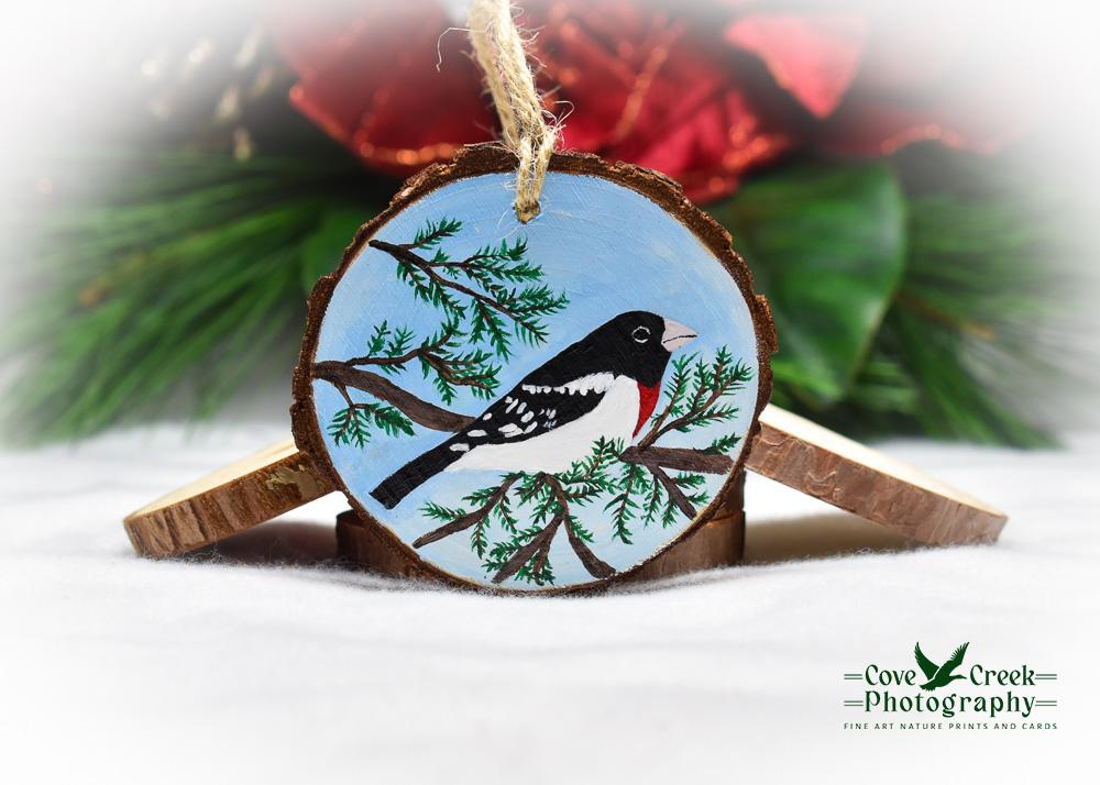 A wood slice Christmas ornament with a hand-painted rose-breasted grosbeak available for purchase at covecreekphotography.com.