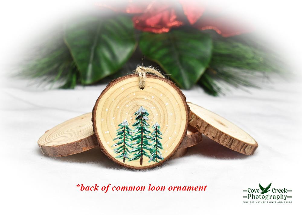 Three hand-painted evergreen trees on the back of a common loon wood slice ornament.