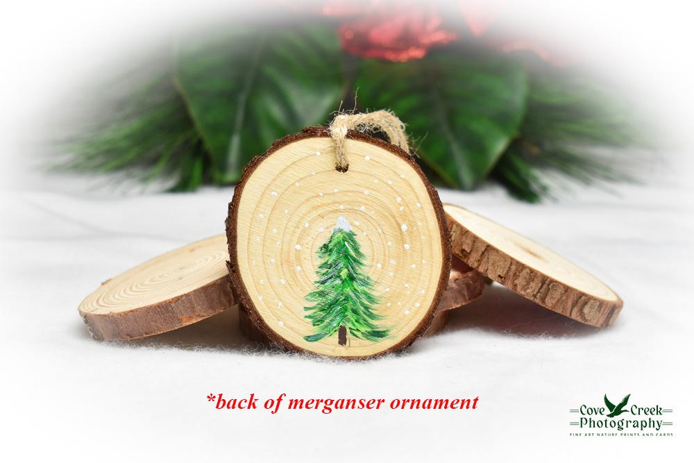 The back of a hooded merganser wood slice ornament with a hand-painted evergreen tree.