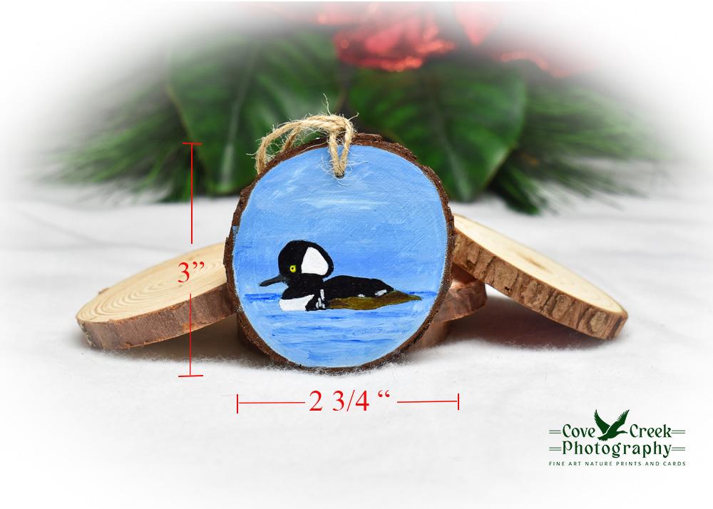 A hand-painted hooded merganser on a wood slice ornament with a diagram of ornament measurements.