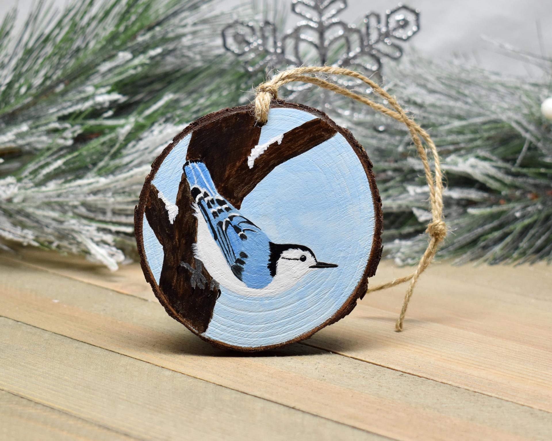 A 3.5 inch round wood slice Christmas ornament with a hand-painted white-breasted nuthatch perched on the side of a tree at Cove Creek Photography.