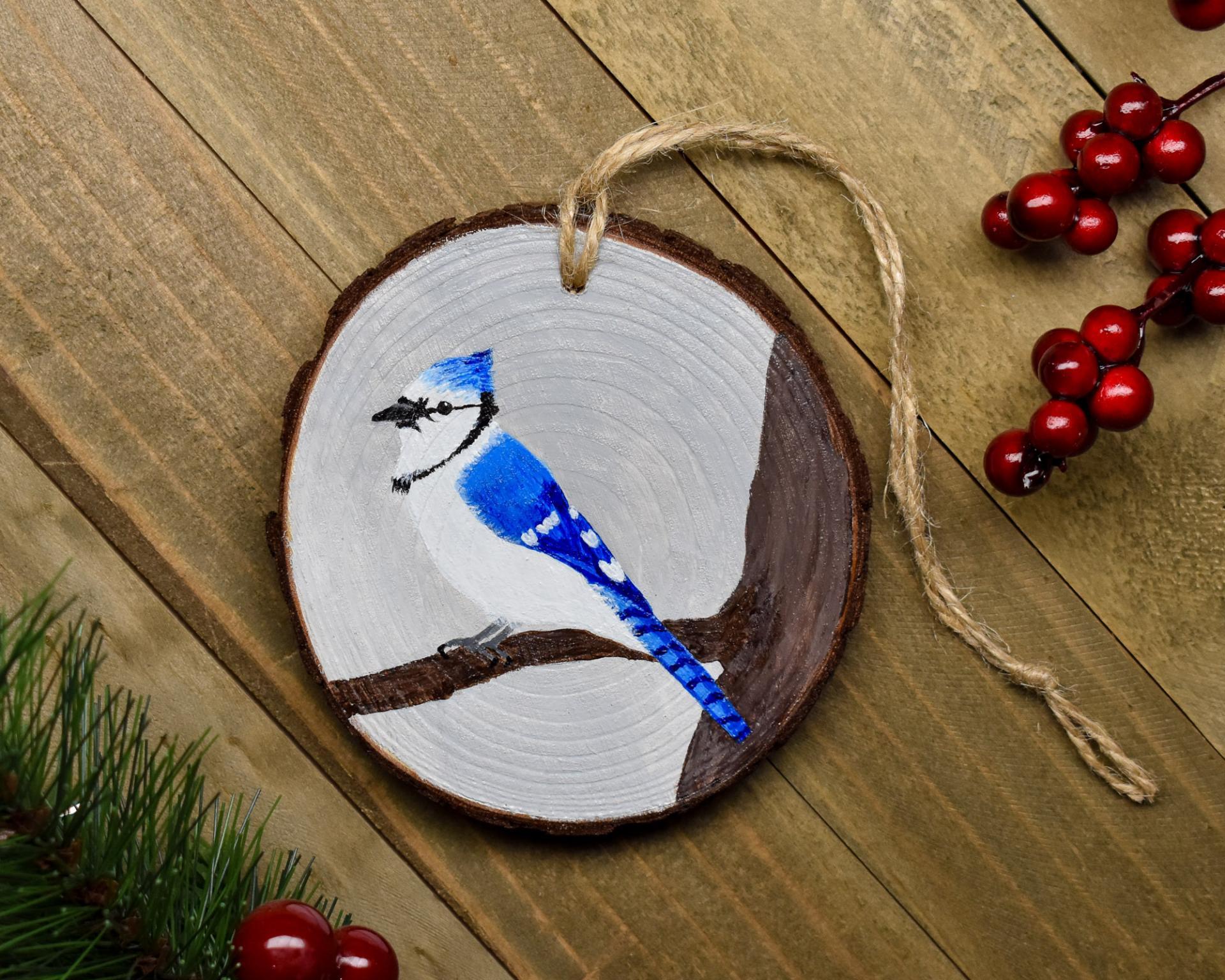 A handmade wood slice ornament with a hand-painted blue jay at covecreekphotography.com.