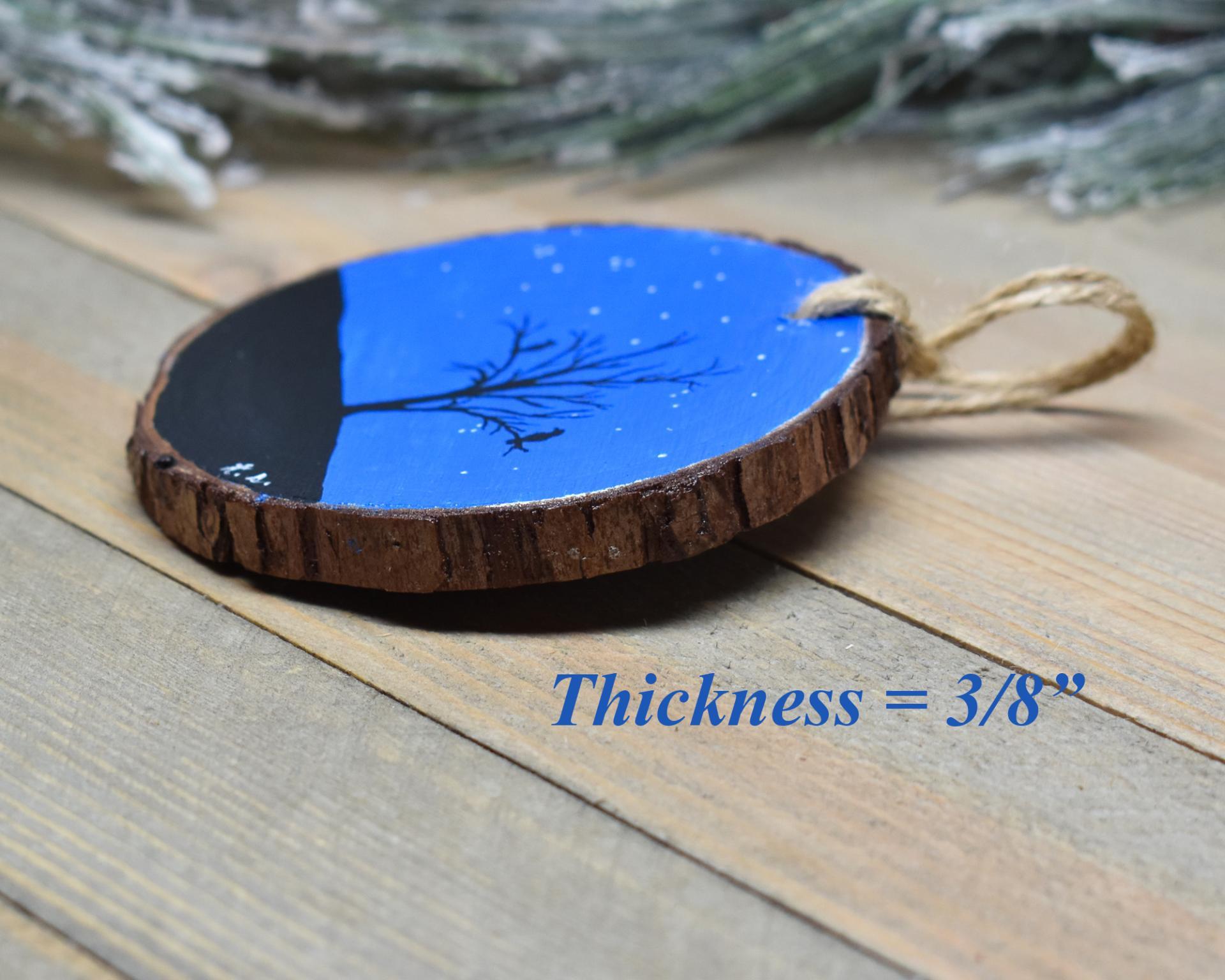 An image of the side of a hand-painted wood slice ornament wth the 3/8 inch thickness displayed in blue font.