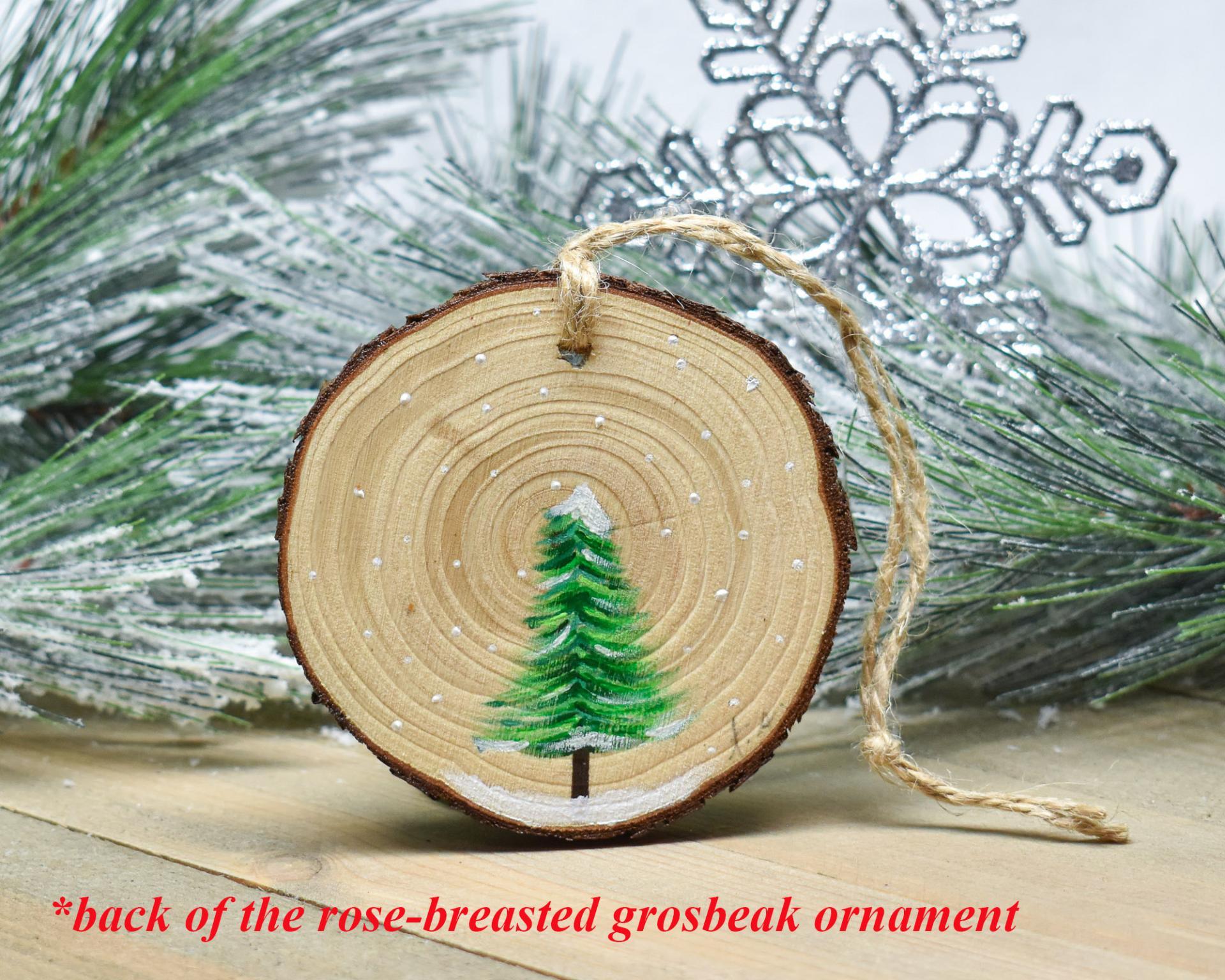 The back of a handmade wood slice ornament with hand-painted evergreen tree in snow at Cove Creek Photography.