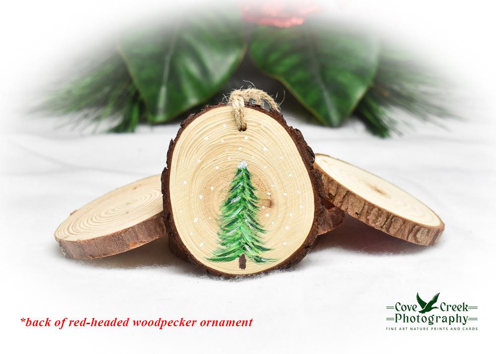 A hand-painted evergreen tree in the snow on a wood slice ornament.