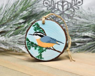 A wood slice Christmas ornament with an acrylic painting of a red-breasted nuthatch at covecreekphotography.com.