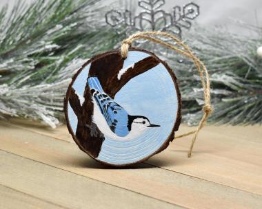A 3.5 inch round wood slice Christmas ornament with a hand-painted white-breasted nuthatch perched on the side of a tree at Cove Creek Photography.