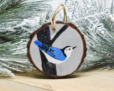 A hand-painted white-breasted nuthatch in the snow on a wood slice at Cove Creek Photography.