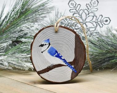 A blue jay perched on a bare tree branch that is hand-painted on a wood slice ornament at Cove Creek Photography.